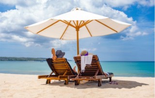 Two people on a sunny beach resting under an umbrella